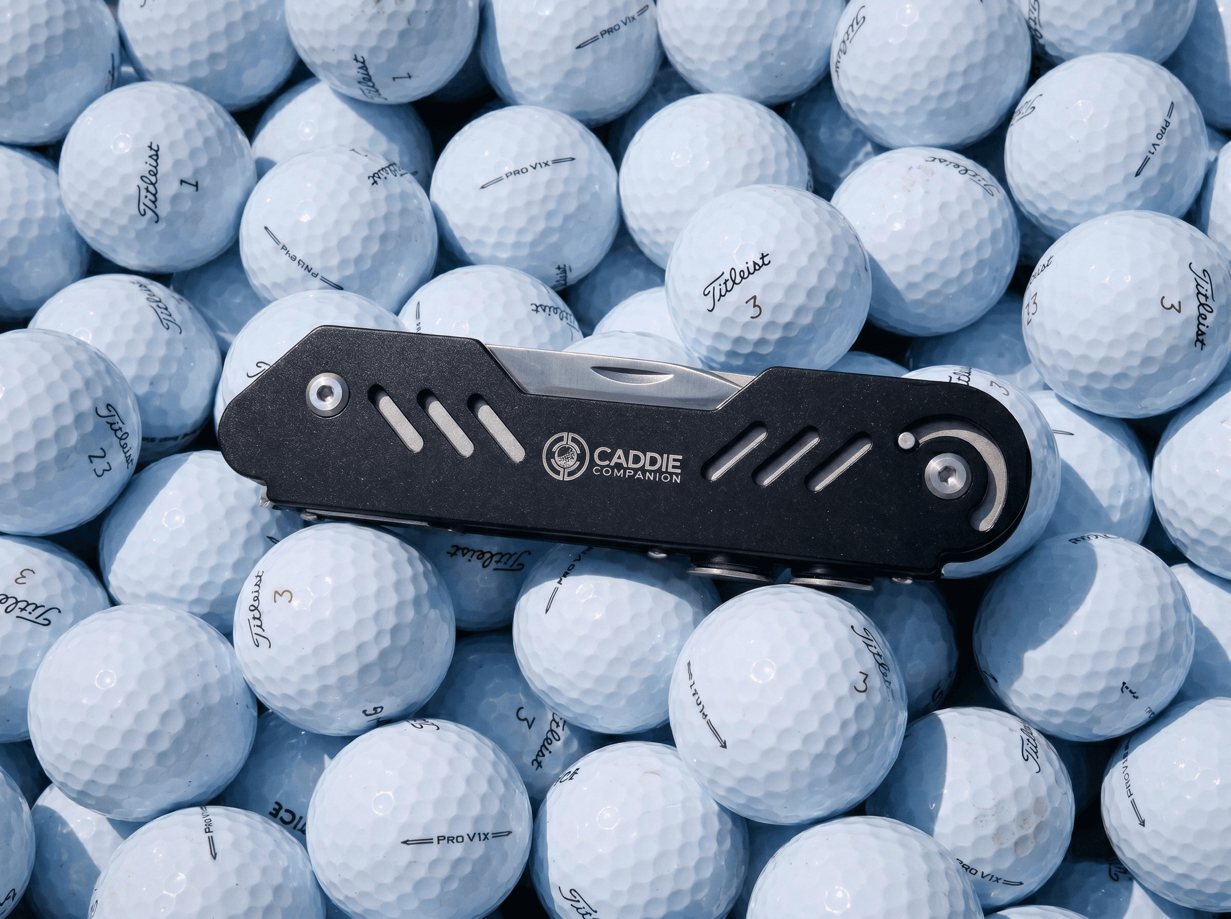 Built to live in the bag The black Caddie Companion multi-tool laid across a bed of golf balls