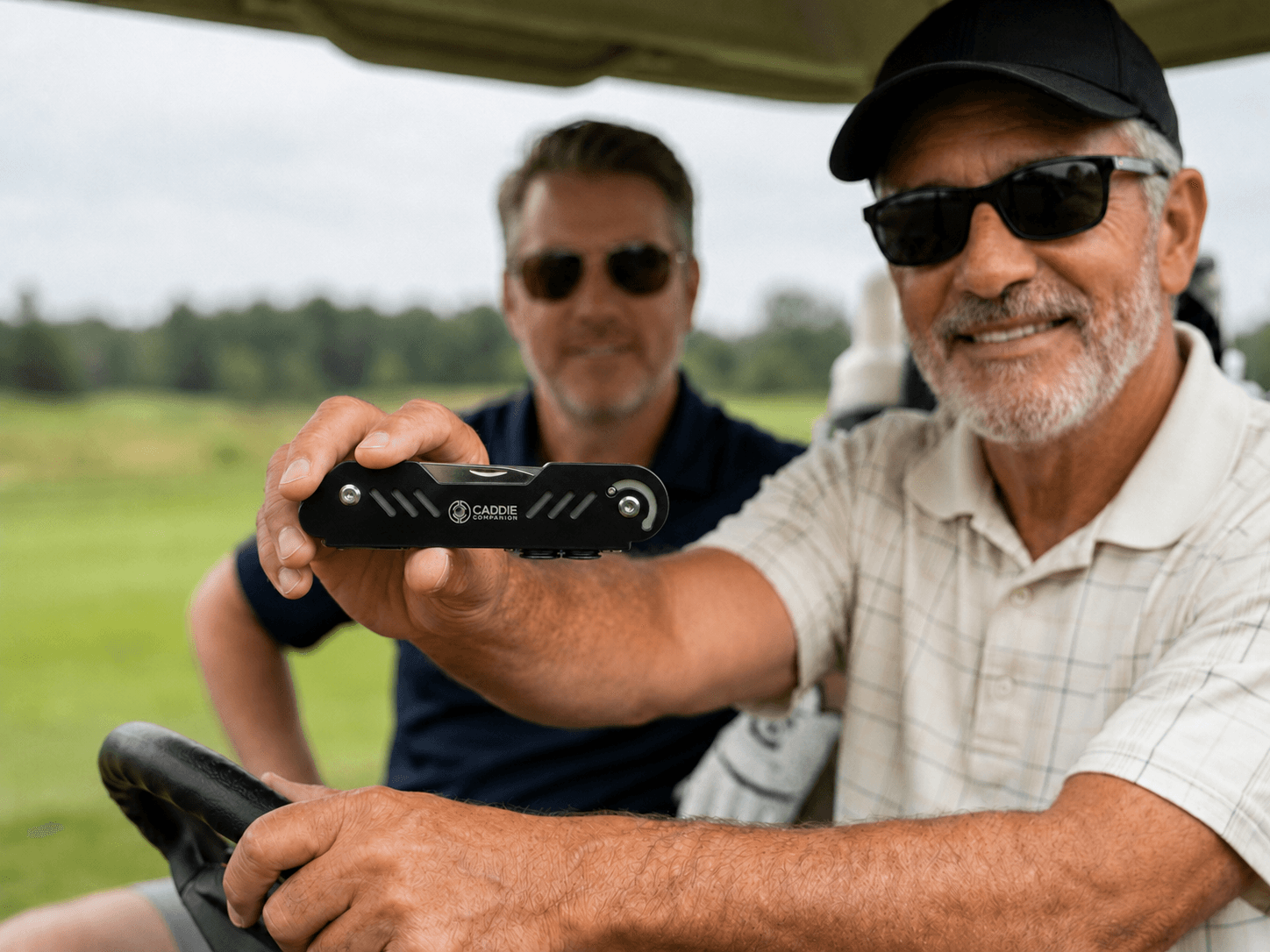 Made for the people who actually play the course A smiling golfer in a cart holding up the black Caddie Companion multi-tool, playing partner beside him